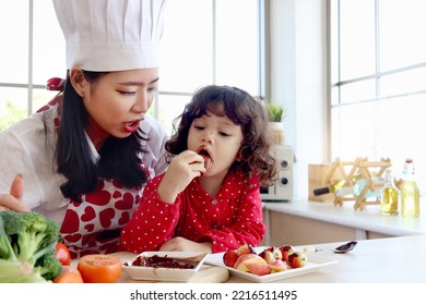 Happy Smiling Cute Little Girl Eating Chocolate And Face Covered In Chocolate, Adorable Child Daughter Enjoy Spending Time Together With Beautiful Young Mother. Love Warmth Family Mom And Kid Concept.