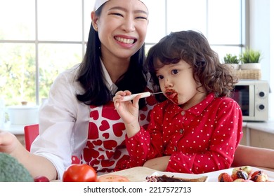 Happy Smiling Cute Little Girl Eating Chocolate And Face Covered In Chocolate, Adorable Child Daughter Enjoy Spending Time Together With Beautiful Young Mother. Love Warmth Family Mom And Kid Concept.