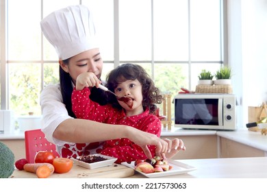 Happy Smiling Cute Little Girl Eating Chocolate And Face Covered In Chocolate, Adorable Child Daughter Enjoy Spending Time Together With Beautiful Young Mother. Love Warmth Family Mom And Kid Concept.