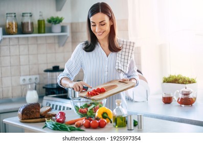 Happy smiling cute woman is preparing a fresh healthy vegan salad with many vegetables in the kitchen at home and trying a new recipe - Powered by Shutterstock