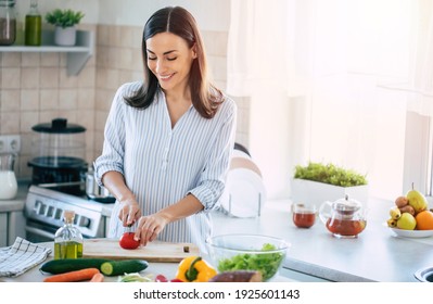 Happy Smiling Cute Woman Is Preparing A Fresh Healthy Vegan Salad With Many Vegetables In The Kitchen At Home And Trying A New Recipe