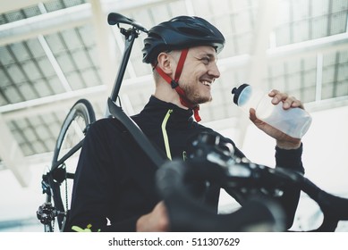 Happy smiling cyclist man drinking water while resting after intensive driving a bike, cheerful young male cyclist holding road bike on shoulder, after sunny morning workout, healthy, sport lifestyle
