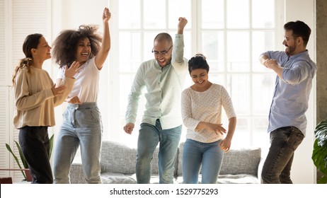 Happy smiling diverse friends dancing to favorite music at home party, having fun on weekend, laughing and singing, funny activity, celebrating indoors, spending free time together