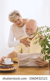 Happy, Smiling Elderly Couple Reading A Newspaper Together And Hugging