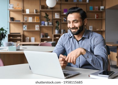 Happy Smiling Ethnical Indian Businessman Having Online Virtual Meeting Call On Laptop Looking At Screen Sitting At Table In Coworking Creative Office, Professional Manager Talking To Employees.