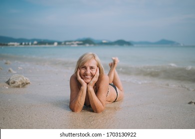 Happy Smiling Excited Elderly Senior Woman Tourist Playing In Water And Swimming In The Big Waves On The Ocean Sea Beach. Traveling Along Asia, Active Lifestyle Concept.