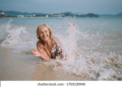 Happy Smiling Excited Elderly Senior Woman Tourist Playing In Water And Swimming In The Big Waves On The Ocean Sea Beach. Traveling Along Asia, Active Lifestyle Concept.