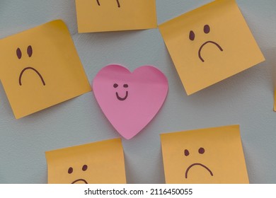 Happy Smiling Face Amongst Lots Of Sad Faces. Hiding Depression, Mental Health Issues Or Anxiety Concept. Two Faces Concepts Background. Pretending Faking It.