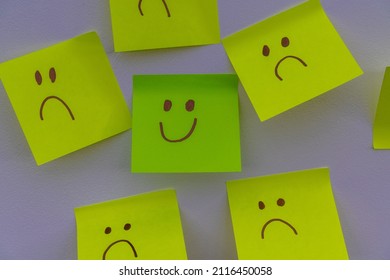 Happy Smiling Face Amongst Lots Of Sad Faces. Hiding Depression, Mental Health Issues Or Anxiety Concept. Two Faces Concepts Background. Pretending Faking It.