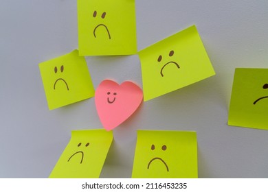 Happy Smiling Face Amongst Lots Of Sad Faces. Hiding Depression, Mental Health Issues Or Anxiety Concept. Two Faces Concepts Background. Pretending Faking It.