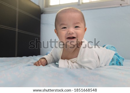 Happy smiling face of Chinese baby boy on tummy time on bed. Newborn child relaxing in bed