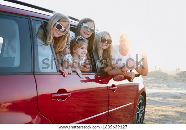 Happy smiling family with\
daughters in the car with sea background. Portrait of a smiling\
family with children at beach in the car. Holiday and travel\
concept \
