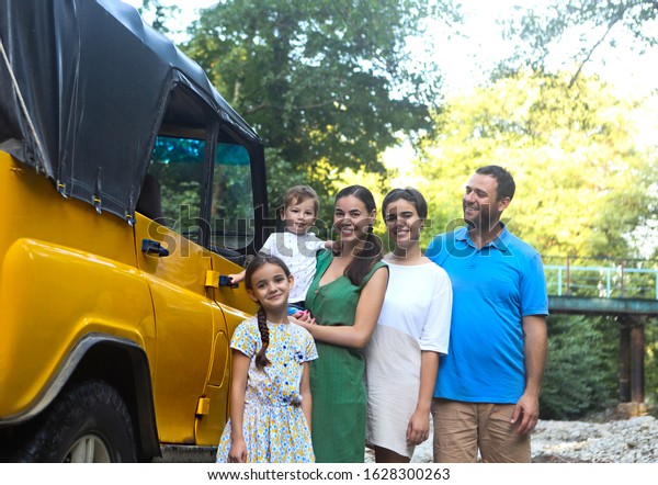 Happy smiling family with\
kids by the car with mountain river background. Portrait of a\
smiling family with children in country near the car. Holiday and\
travel concept 