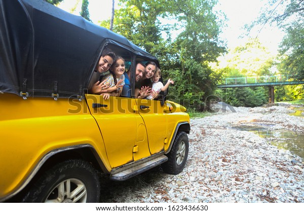 Happy smiling family with\
kids in the car with mountain river background. Portrait of a\
smiling family with children in country in the car. Holiday and\
travel concept 