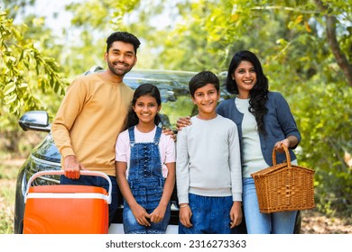 Happy smiling family with sibling kids standing in front of car for picnic by looking camera during holiday travel - concept of joyful lifestyle, family time and freedom