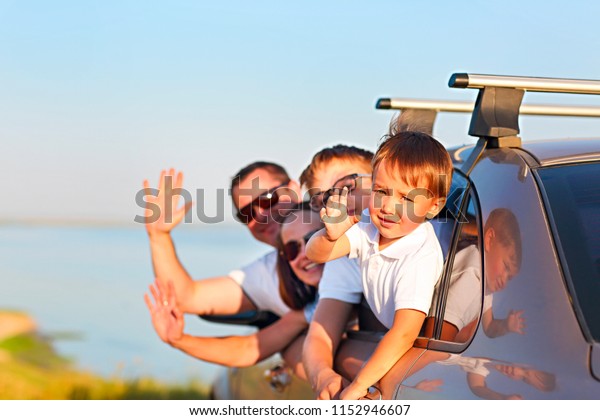 Happy smiling family with two\
kids sitting in the car by the sea. Portrait of a smiling family\
with two children at beach in the car. Holiday and travel\
concept