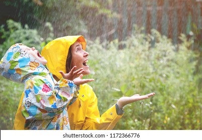 Happy Smiling Family Under Summer Rain. Smiling Mother And Little Child Girl Have Fun Time While Playing Outdoors Under Autumn Shower. Kid Without Umbrella And In Waterproof Coat