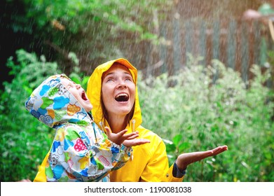 Happy Smiling Family Under Summer Rain. Smiling Mother And Little Child Girl Have Fun Time While Playing Outdoors Under Autumn Shower. Kid Without Umbrella And In Waterproof Coat