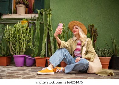 Happy smiling fashionable woman takes selfie. Model wearing stylish summer outfit, posing near green  color house with natural plants. Copy, empty space for text
 - Shutterstock ID 2164261475