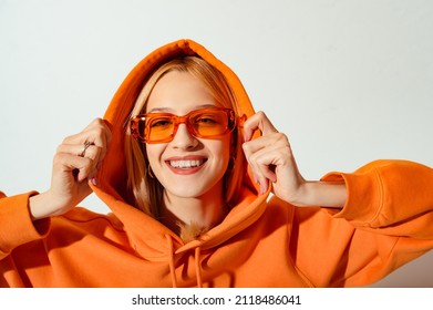 Happy smiling fashionable woman wearing trendy orange color sunglasses, hoodie posing on white background. Close up studio portrait. Copy, empty space for text