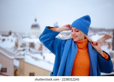 Happy smiling fashionable woman wearing trendy blue winter coat, knitted beanie hat, woolen scarf, orange turtleneck sweater, posing outdoor. Copy, empty space for text - Powered by Shutterstock