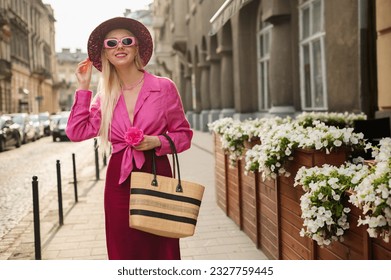 Happy smiling fashionable woman wearing trendy summer outfit with hat, pink sunglasses, linen shirt, skirt, holding straw wicker bag, walking in street of European city. Copy, empty space for text - Powered by Shutterstock