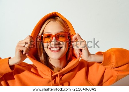 Happy smiling fashionable woman wearing trendy orange color sunglasses, hoodie posing on white background. Close up studio portrait. Copy, empty space for text