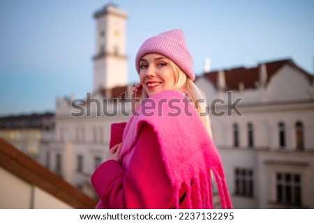 Happy smiling fashionable woman wearing trendy total pink outfit with knitted beanie hat, woolen fringed scarf, coat, posing outdoor. Copy, empty space for text