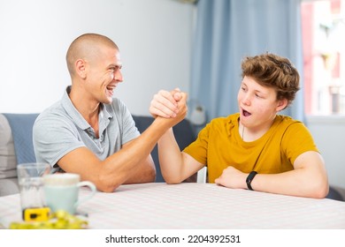 Happy Smiling Father And Son Arm Wrestling At Home. Fatherhood Concept