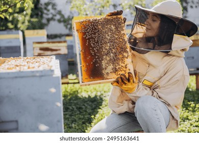 Happy smiling female Beekeeper in protective suit holding honeybee frame with bees at apiary - Powered by Shutterstock