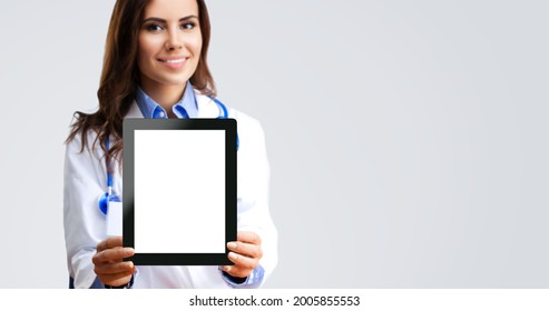 Happy Smiling Female Doctor Showing Tablet Pc Touchpad Ipad With Copy Space For Imaginary Or Text, Over Grey Background. Medical Care Concept. Selective Focus. 