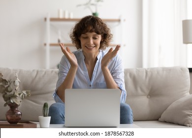 Happy Smiling Female Pc User Sit On Couch Splash Hands In Delight Read Good News On Screen. Excited Young Woman Enjoy Perfect Work Of New Browser App Get Positive Answer From Bank On Request For Loan