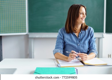 Happy Smiling Female Teacher Or Mature Student Sitting Working In The Classroom On Paperwork Looking To The Side With A Smile