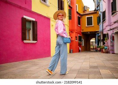 Happy smiling female traveler wearing stylish hat, glasses, pink shirt, wide leg trousers, walking, posing near colorful houses in street. Travel, tourism, vacation, fashion, lifestyle conception - Shutterstock ID 2182099141