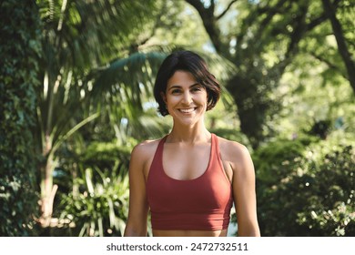 Happy smiling fit sporty active slim confident young Hispanic woman wearing sportswear top enjoying summer sunny day looking at camera standing in green nature park or forest. Portrait. - Powered by Shutterstock