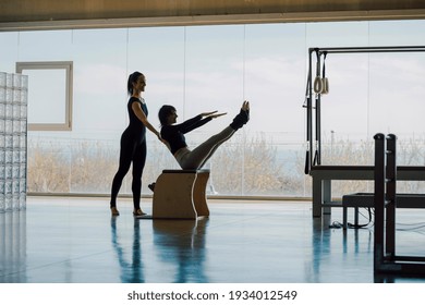 Happy Smiling Fitness instructor and student working out in a big gymnasium, Pilates health club, with wide windows and outside views. Personal trainer correcting posture, helping client with exercise - Powered by Shutterstock