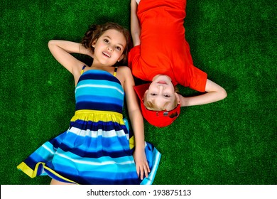 Happy Smiling Girl And Boy In Bright Summer Clothes Lying On A Grass. Children.