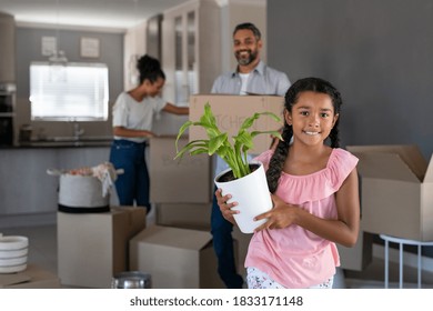 Happy Smiling Girl Holding Plant In New Home While Indian Father Watching Her. Portrait Of Cute Multiethnic Daughter Feeling Excited In New House While Looking At Camera. 