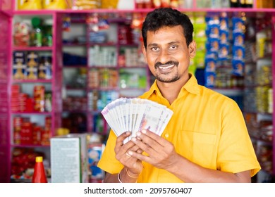 Happy smiling Groceries or Kirana Merchant showing stack of money by looking camera - concept of Successful small businesses and making money.