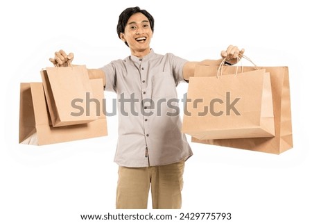 Happy smiling handsome Asian man carrying and showing shopping bags to celebrate Eid Mubarak Idul Fitri