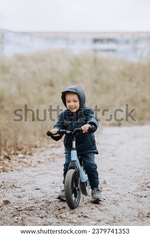Happy smiling handsome child, preschool boy rides fast on a blue balance bike, bicycle without wheels on a road with a slope outdoors in autumn. Photography, portrait, childhood concept, sports.