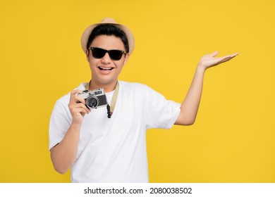 Happy Smiling Handsome Young Asian Male Tourist With Hand Open Gesture And Camera Isolated On Colorful Yellow Background