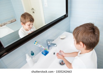 Happy Smiling Healthy Small Kid In White Shirt Wash His Hands Under Fresh Water In Bright Blue Bathroom At Home During Morning Hygienic Procedure