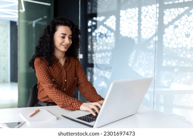 Happy and smiling hispanic businesswoman typing on laptop, office worker with curly hair happy with achievement results, at work inside office building - Powered by Shutterstock