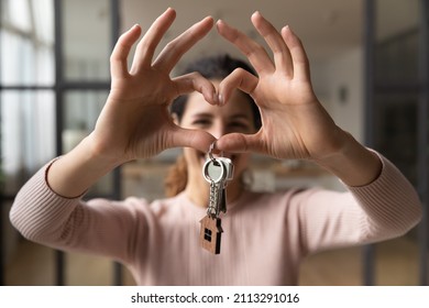 Happy smiling homeowner woman pose in living room hold keys from new first own house while makes heart love symbol with joined fingers. Accommodations apartment for newly-weds, dating services concept