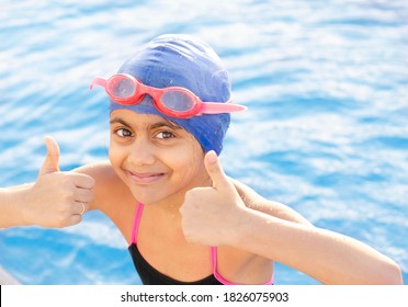 Happy And Smiling Indian Girl Child   Swimming In The Pool Showing Victory Sign ,wearing Swimming Cap And Goggles..