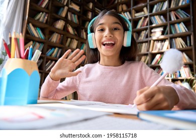 Happy Smiling Indian Latin Student Waiving Hand To Teacher And Pupils On Online Practice Classes In Virtual School. Web Camera View Of Spanish Girl Wearing Headphones Sitting At Home Classroom.