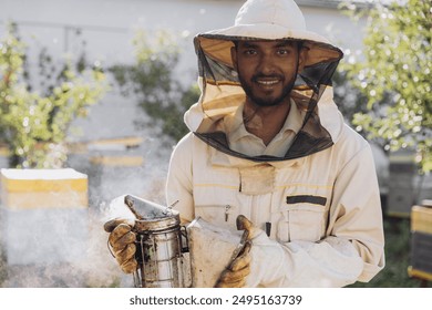 Happy smiling Indian male Beekeeper smoking honey bees with bee smoker on the apiary - Powered by Shutterstock