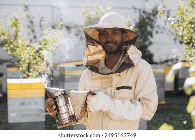 Happy smiling Indian male Beekeeper smoking honey bees with bee smoker on the apiary - Powered by Shutterstock