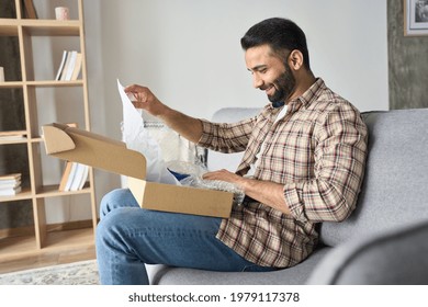 Happy smiling indian man opening box with ordered goods gifts, presents at home on couch. Online shopper male customer opening online shop parcel. International delivery service concept.